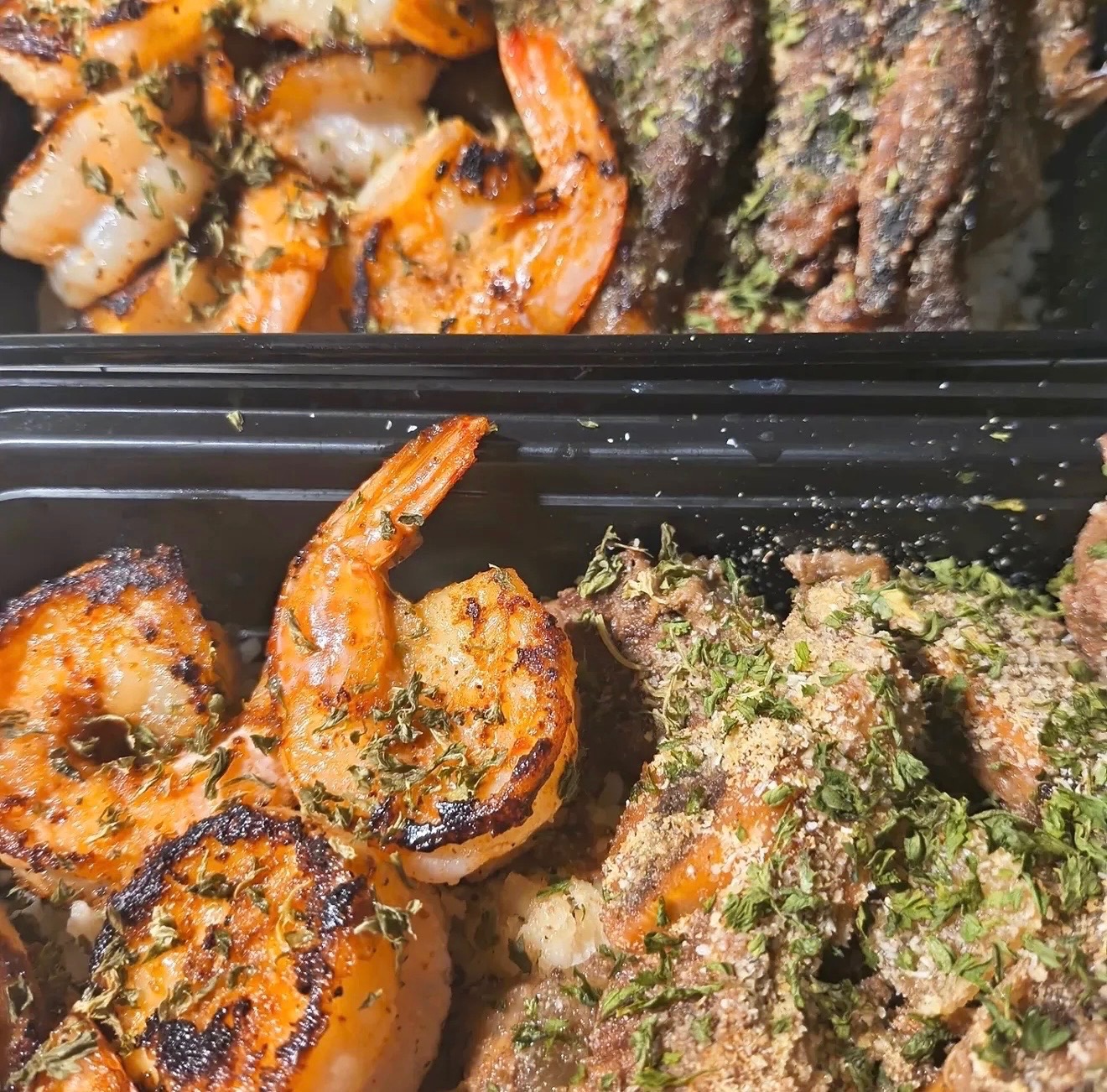 Grilled jumbo shrimp and seasoned blackened ribs in catering trays, dusted with parsley