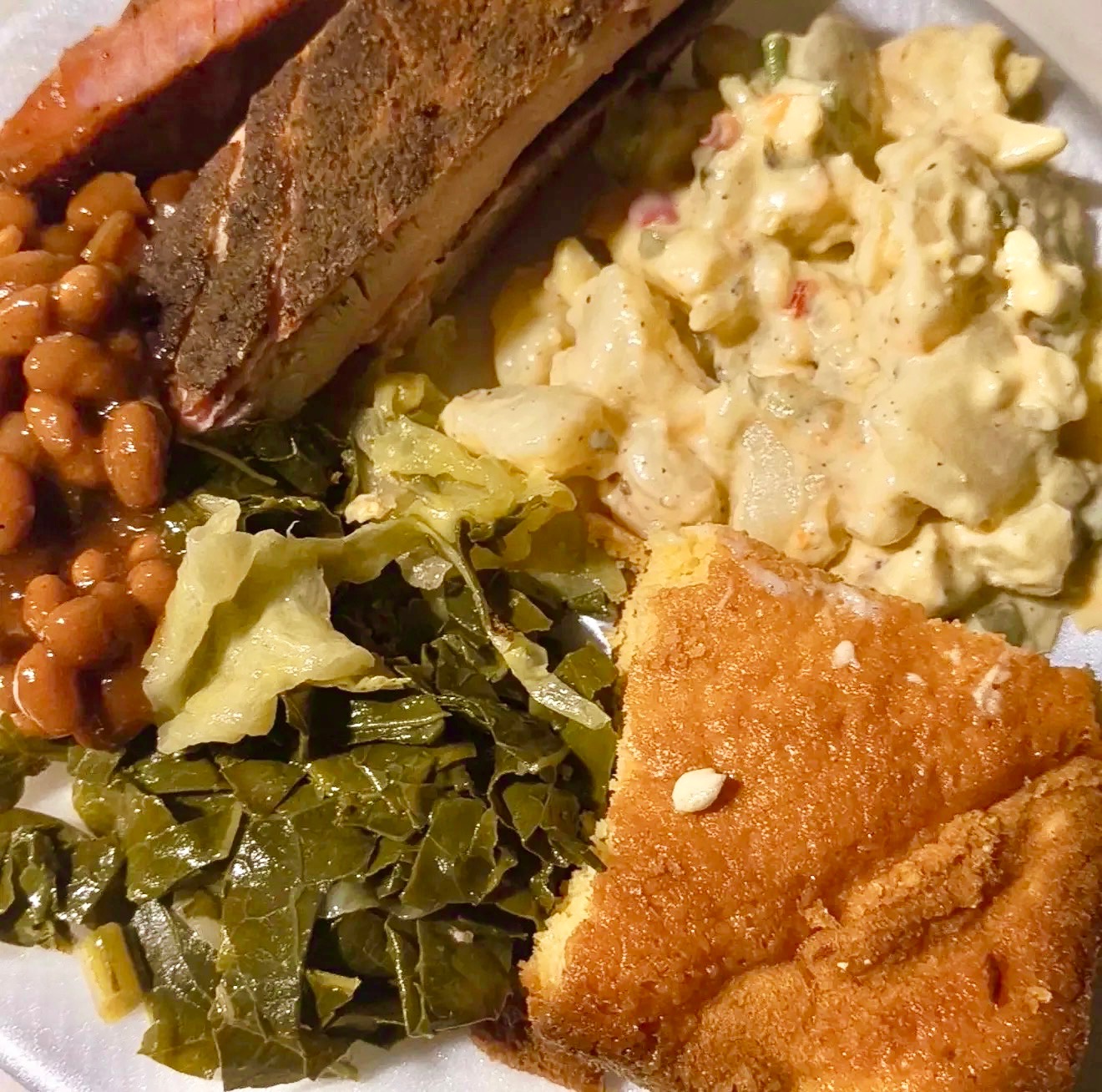 Smoked BBQ ribs plated with baked beans, collard greens, potato salad, and cornbread